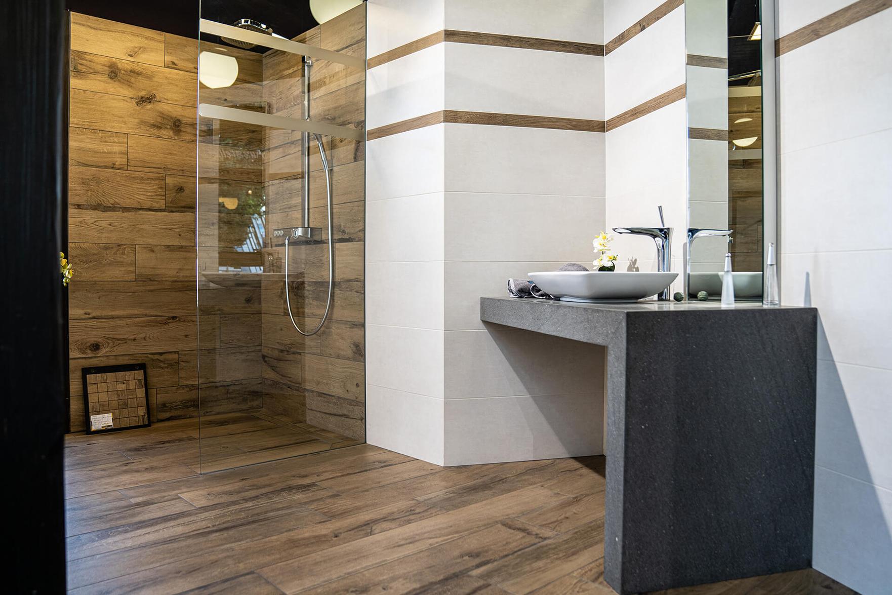 Badezimmer mit Holzoptik-Fliesen, bodengleicher Dusche und Waschtisch in der Ausstellung Bonn